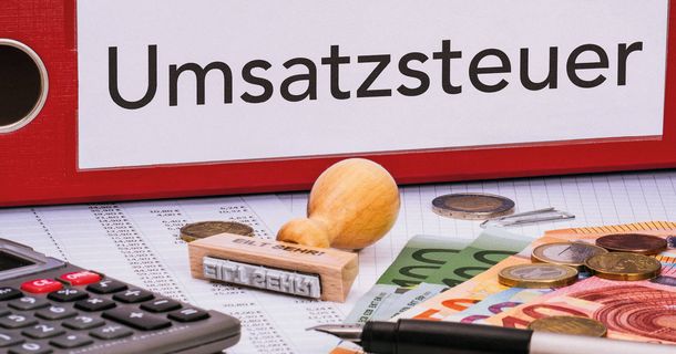 Ein Umsatzsteuer Ordner liegt auf dem Tisch mit einer Stempel, einem Taschenrechner und Bargeld.