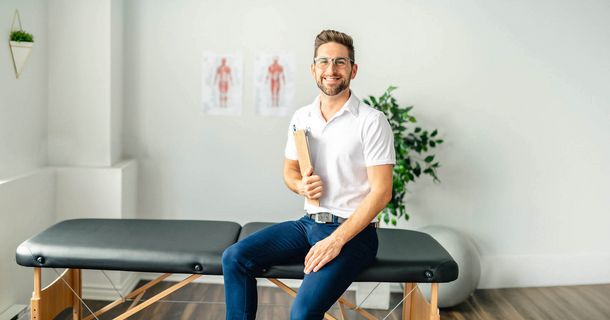 Physiotherapeut sitzt auf einer Therapieliege