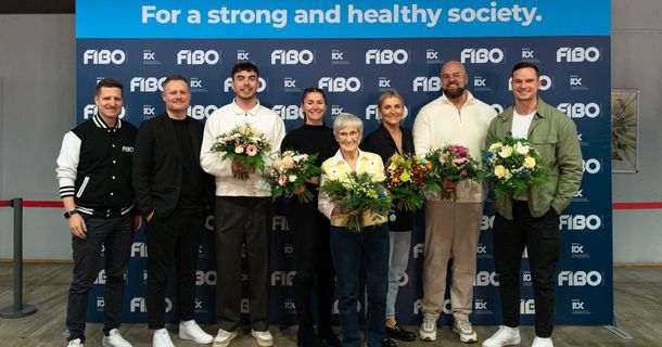 Gruppenbild vor FIBO-Pressewand, einige Personen haben Blumensträuse in der Hand