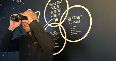 Florian Hempen, sateht vor einer schwarzen Wand und schaut durch ein Fernglas