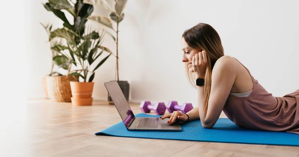 Junge Frau liegt auf Fitnessmatteund schaut in den Laptop