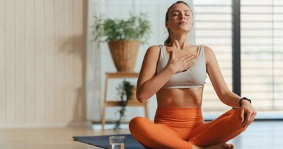 Frau im Schneidersitz atmet tief mit einer Hand auf ihrer Brust