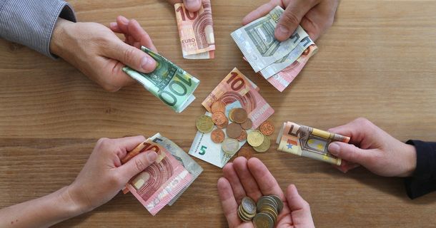 Mehrere Hände mit Geldscheinen und Münzen an einem Tisch