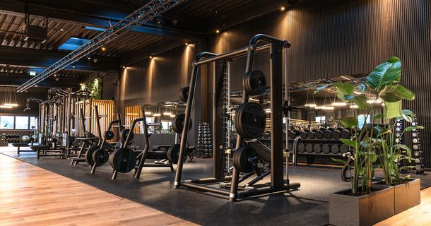 Moderner, hochwertig ausgestatteter Kraftbereich eines Premium-Fitnessclubs mit mattschwarzen Racks, Hanteln und stimmungsvoller Beleuchtung.