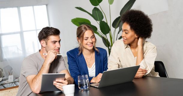 Drei junge Menschen lächelnd vor ihren Laptops