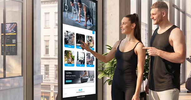 Mann und Frau in Sportkleidung vor einem großen Display von TOUCH:BAY