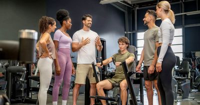 Junger Mann sitzt an einer Brustpresse im Studio, weitere junge Menschen um ihn herum, ein Mann erklärt etwas  IST-Ausbildertag in Stuttgart
