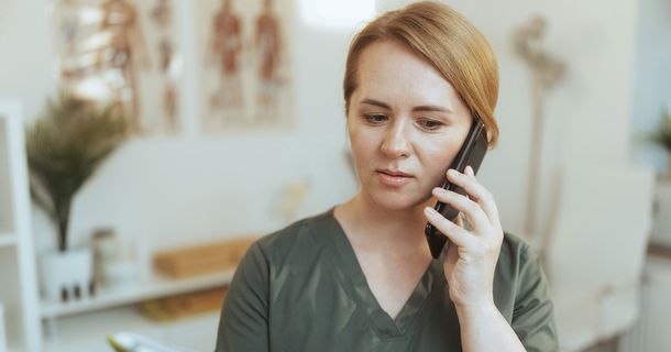 Eine Physiotherapeutin hat ein Telefon in der Hand und telefoniert.