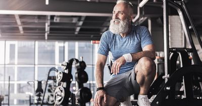 Älterer Mann mit grauem Bart lächelnd und kniend im Gym