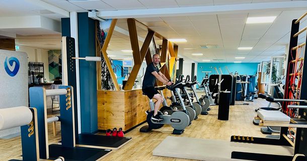 Eine Mitarbeiterin der Vitova Gruppe unterstützt eine trainierende, die auf einem Indoor Cycle sitzt.