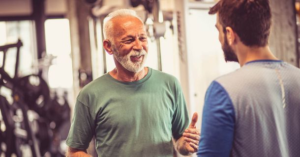 Älterer Mann im Gespräch mit jüngerem Mann im Fitnessstudio