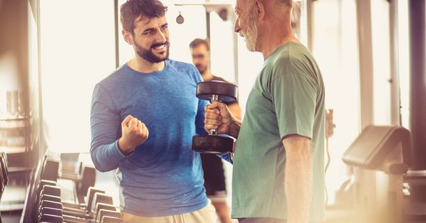 Junger Mann motiviert älteren Mann in einem Fitnessstudio