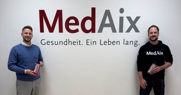 Julian Leppich & Geschäftsführer MedAix Mönchengladbach Dennis Buttermann posieren vor dem MedAix-Logo in der zweiten Praxis in Mönchengladbach