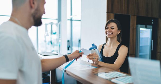Frau checkt bei einem Servicemitarbeiter im Fitnessstudio ein
