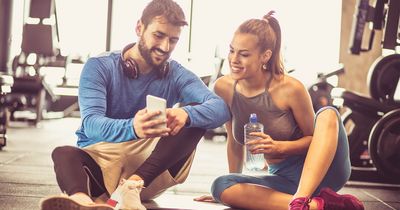 Mann und Frau schauen auf dem Gymboden sitzend auf ein Smartphone