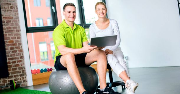Fitnesstrainer auf einem Ball neben einer Fitnesstrainerin