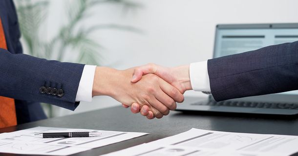 Handschlag über einem Tisch mit Zetteln und Kugelschreiber