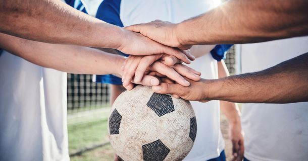 Mehrere Hände übereinander gelegt auf einem Fußball
