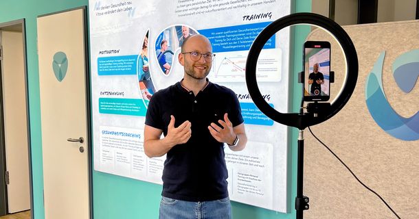 Ein Smartphone hängt an einem Ringlicht und filmt einen Mitarbeiter der Vitova-Gruppe.