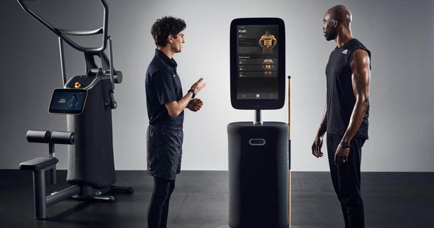 Trainer und Trainierender stehen vor dem Fitness Hub. Im Hintergrund ist ein EGYM-Gerät