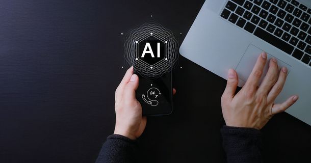 Ein Mensch tippt hält ein Smartphone mit AI Button und tippt etwas auf seinem Laptop ein