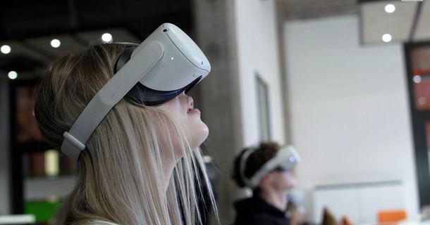 Junge Frau mit VR-Brille, im Hintergrund weitere Person mit VR-Brille