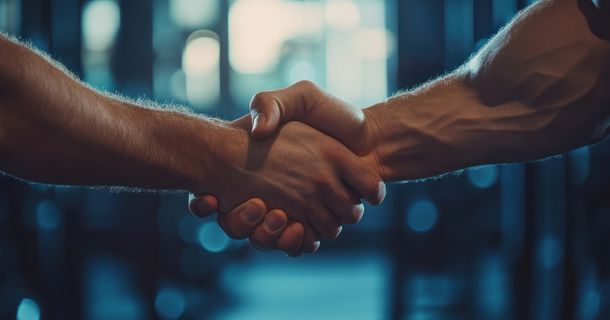 Im Vordergrund sieht man einen Handschlag und im Hintergrund ein verschwommenes Fitnessstudio.