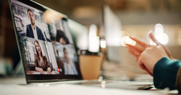 Hände vor Laptop, auf dem mehrere Gesprächsteilnehmer per Video zugeschaltet sind