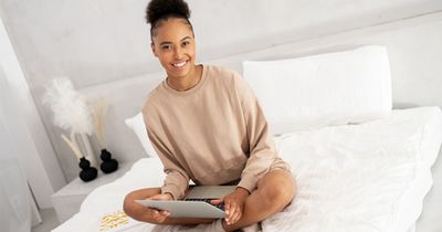 Dunkelhäutige Frau mit einem Laptop auf dem Bett in die Kamera lächelnd