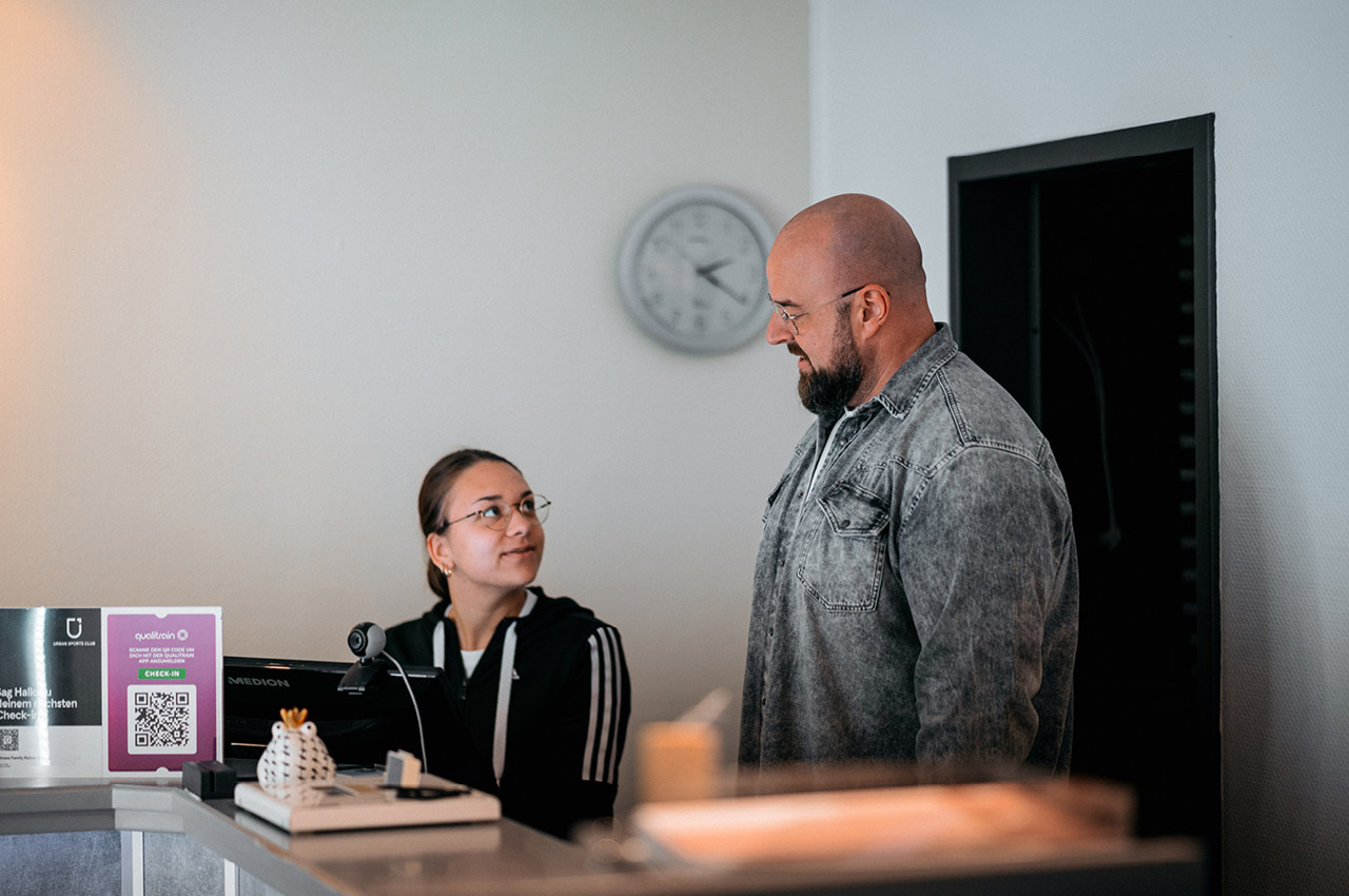 Ein Physiotherapeut spricht mit seiner neuen Mitarbeiterin, die am Empfang sitzt.