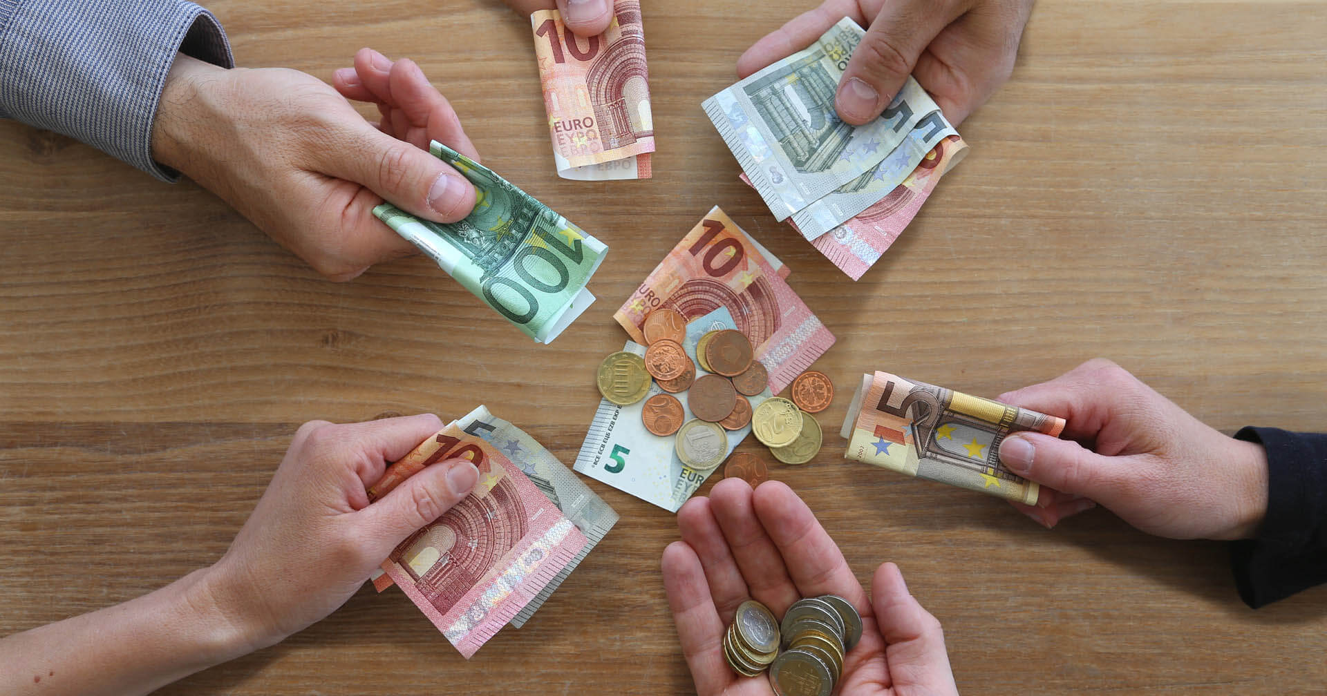 Mehrere Hände mit Geldscheinen und Münzen an einem Tisch