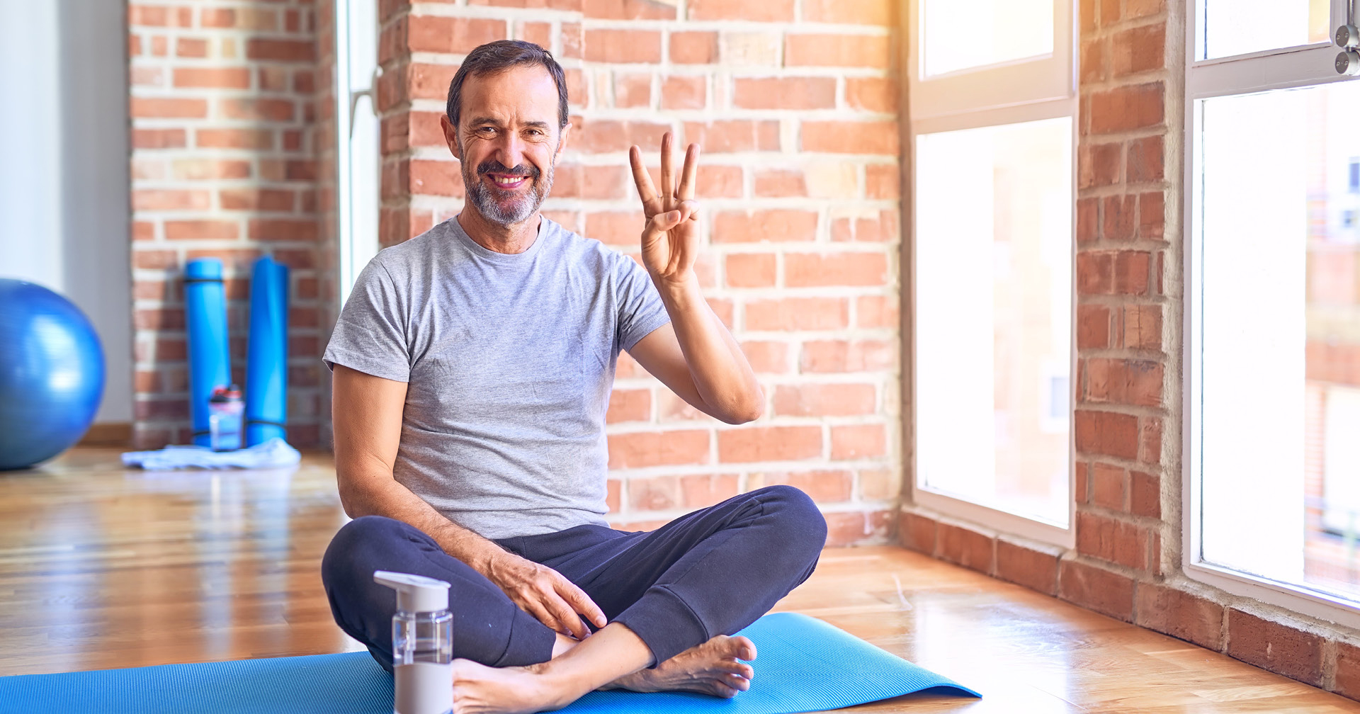 Mann sitzt im Fitnessstudio auf Yogamatte