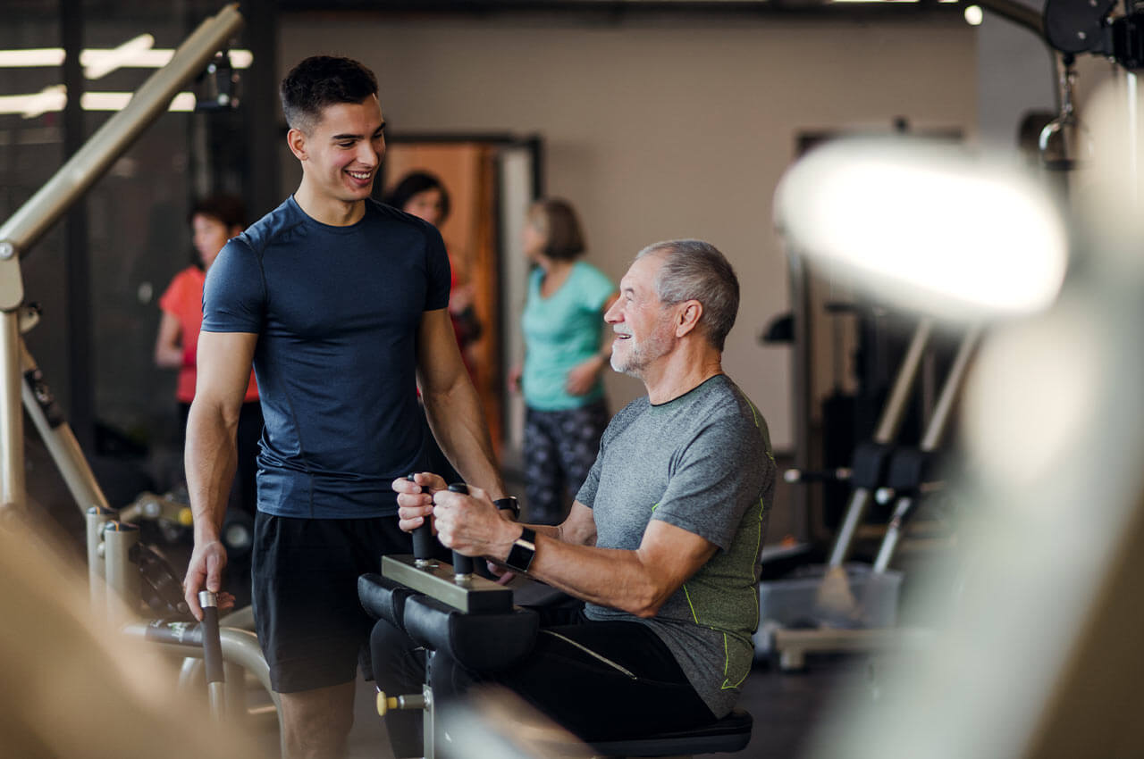 Die Zukunftsfähigkeit und Gesundheit wird auch durch Training bestimmt Älterer mann trainiert an einer Maschine, während sein Trainer zuschaut