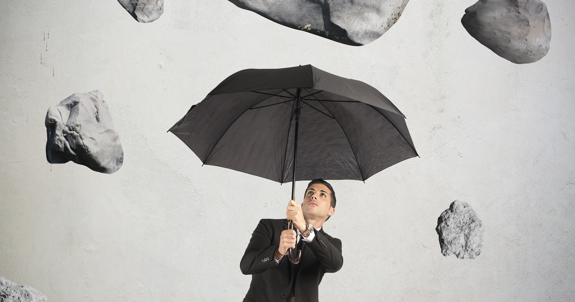 Unternehmer hält einen Regenschirm über sich während Steine vom Himmel fallen