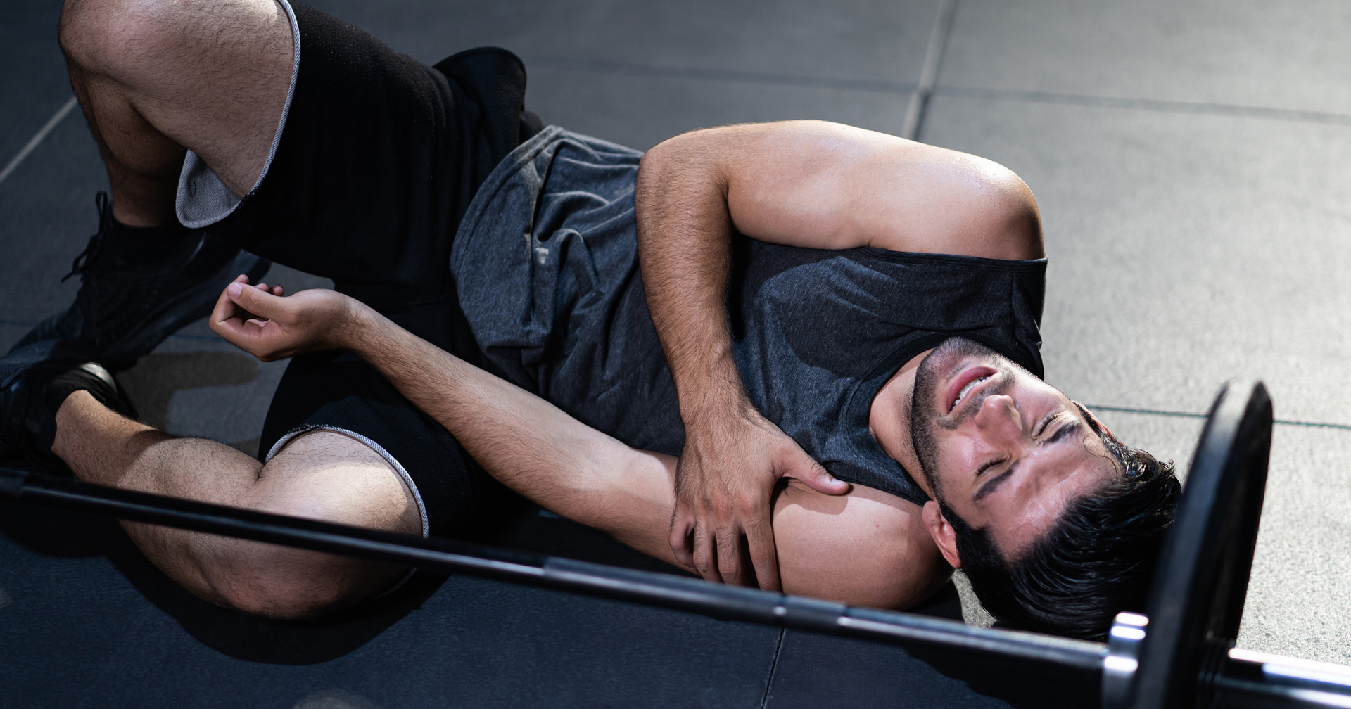 Fitnessstudiomitglied liegt verletzt auf der Trainingsmatte neben einer Langhantel