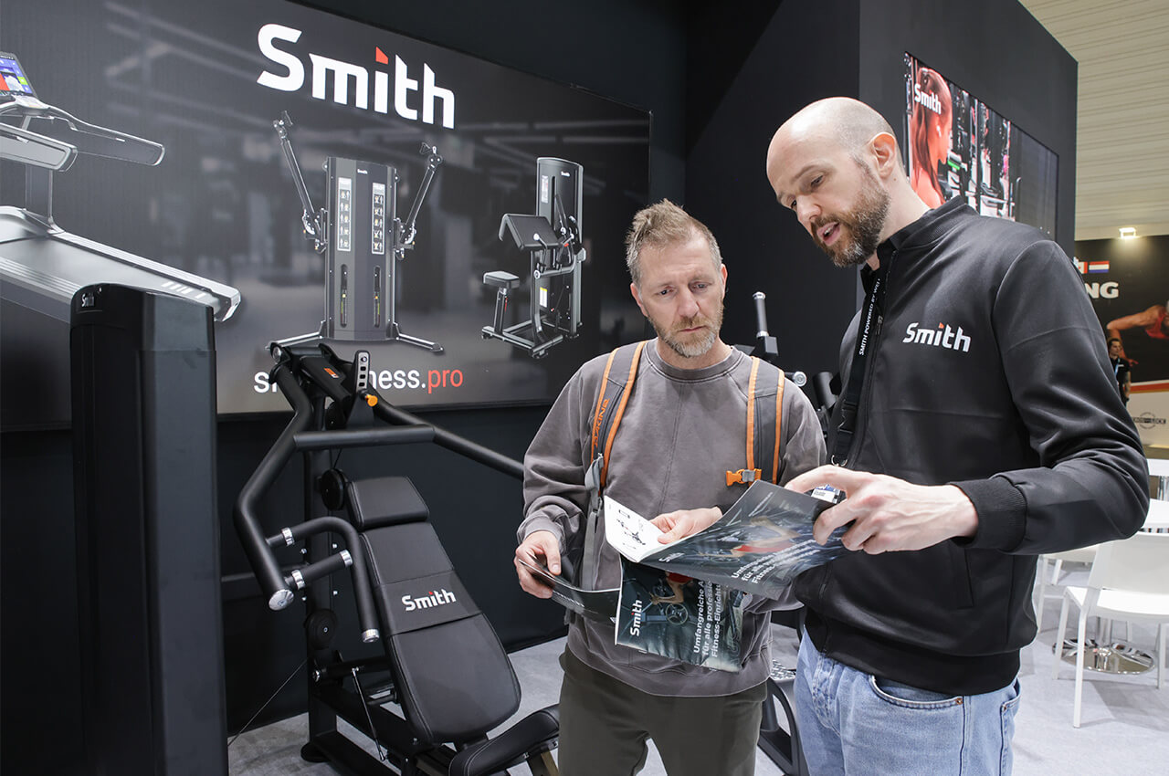 Die Trainingsgeräte von SMITH stießen auf der FIBO auf großes Interesse Alexander Kraus mit einem Kunden vor einem SMITH-Trainingsgerät