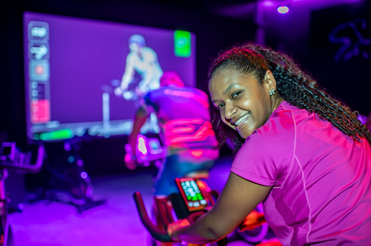 Eine Sportlerin blickt lächelt und sitzt auf einem Indoor Cycle während einer DarkCycling Class.