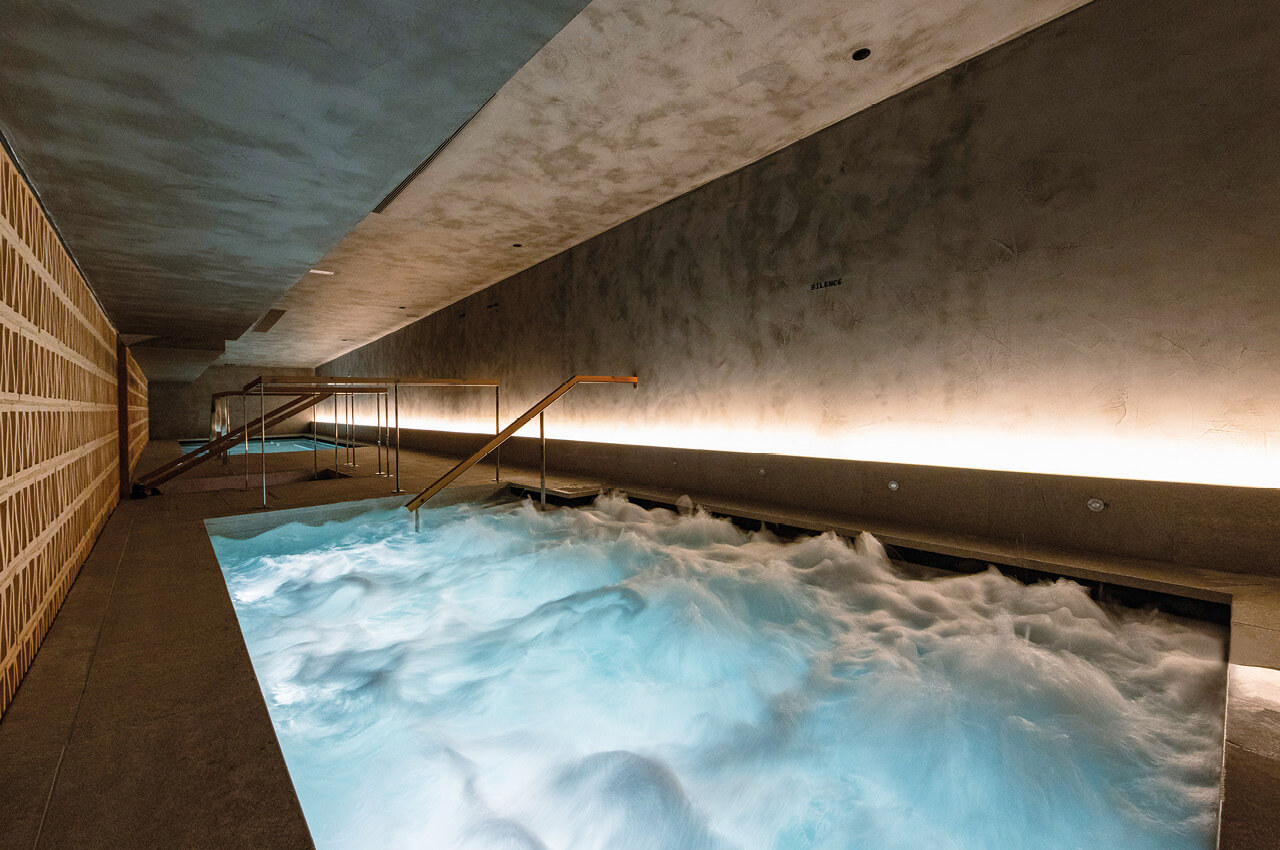 Wellnessbereich mit beleuchtetem Indoor-Pool und Sprudelwasser in modernem, minimalistischem Design.