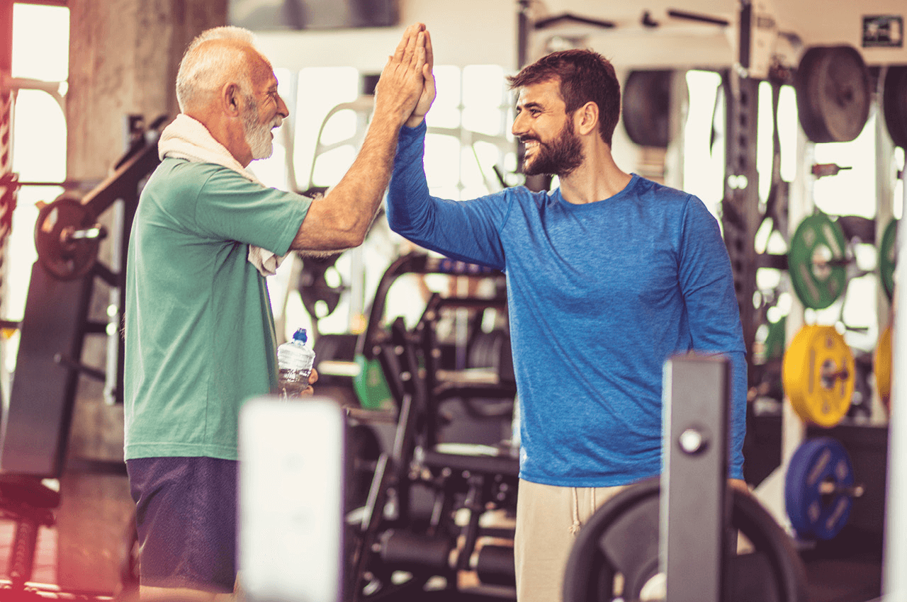 Ein Trainer klatscht, in einem Fitnessstudio, die Hand eines älteren Trainierenden. 