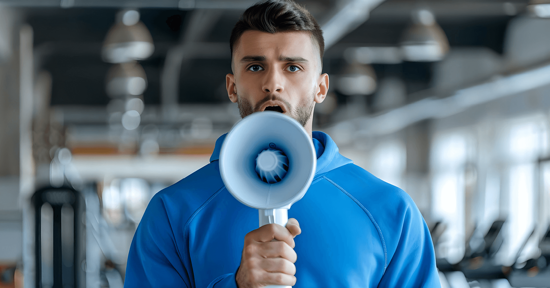 Ein Trainer hat ein Megafon in der Hand und steht in einem Fitnessstudio.