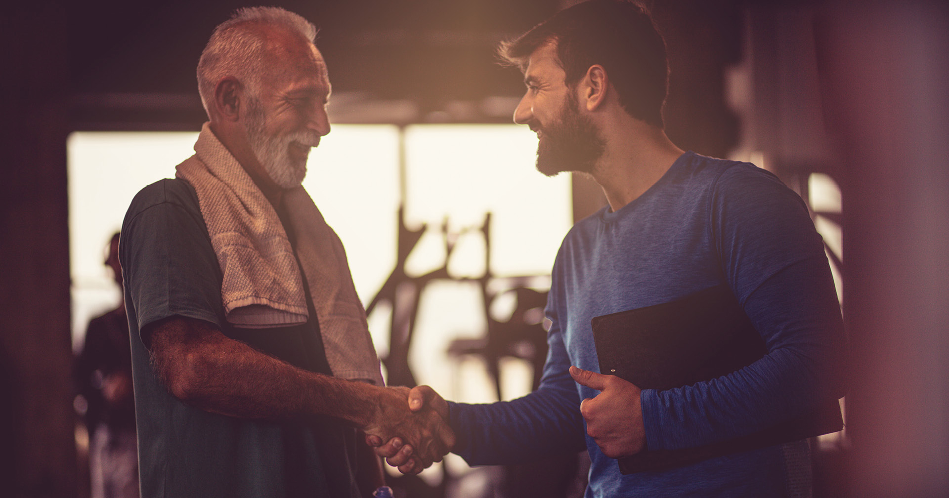 Fitness-Trainer und Mitglied schütteln sich lachend die Hand