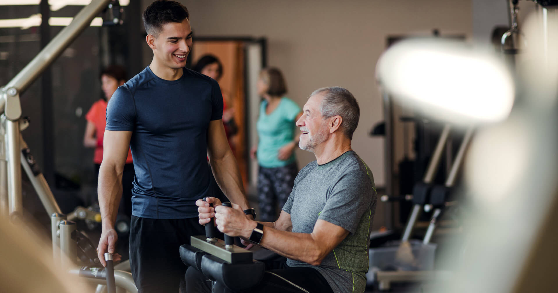 Trainer mit Senior beim Fitnesstraining am Gerät