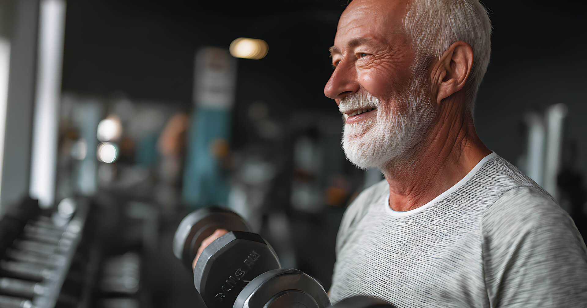 Älterer Mann mit grauem Bart mit Hanteln im Fitnessstudio