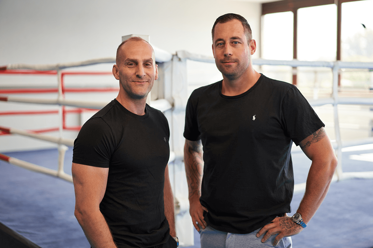Robin Baumann und Falk Berberich stehen nebeneinander in einer Kampfsporthalle.