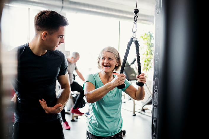 Trainer erklärt Rentnerin eine Übung am Kraftgerät im Medical-Fitness-Club