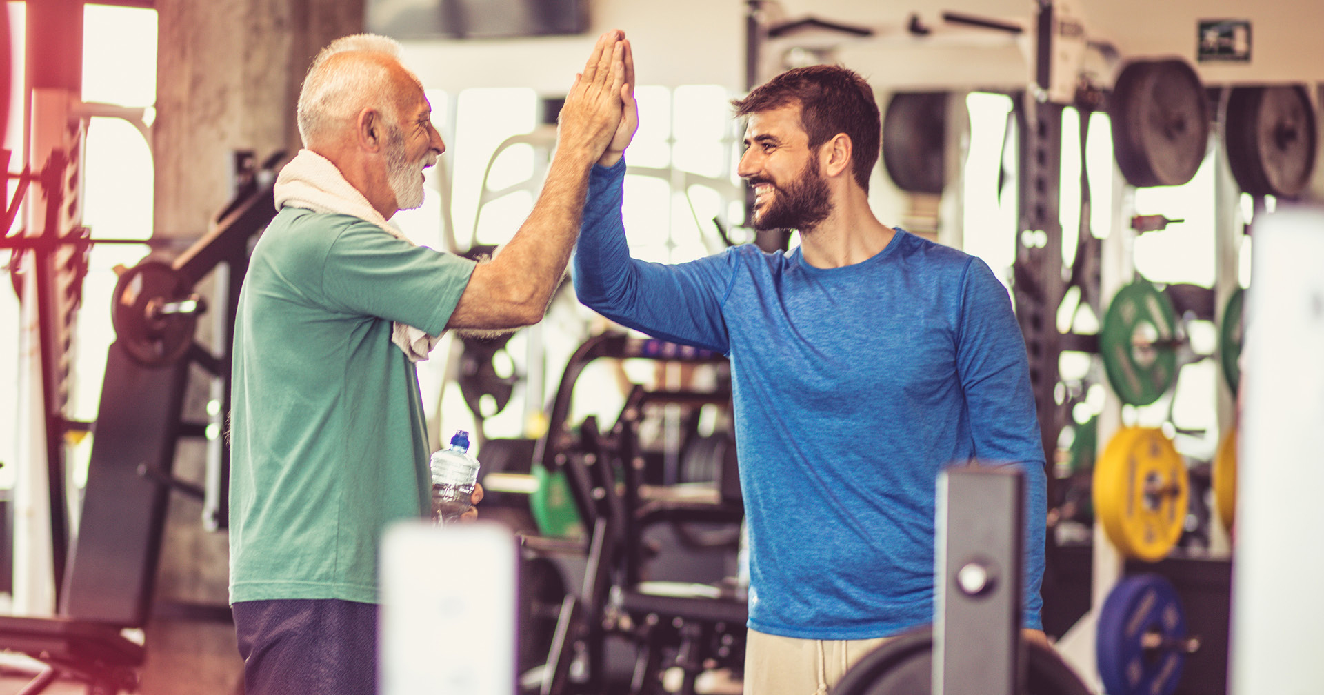 Fitnessstudiomitglied und Fitnesstrainer begrüßen sich mit einem High-Five