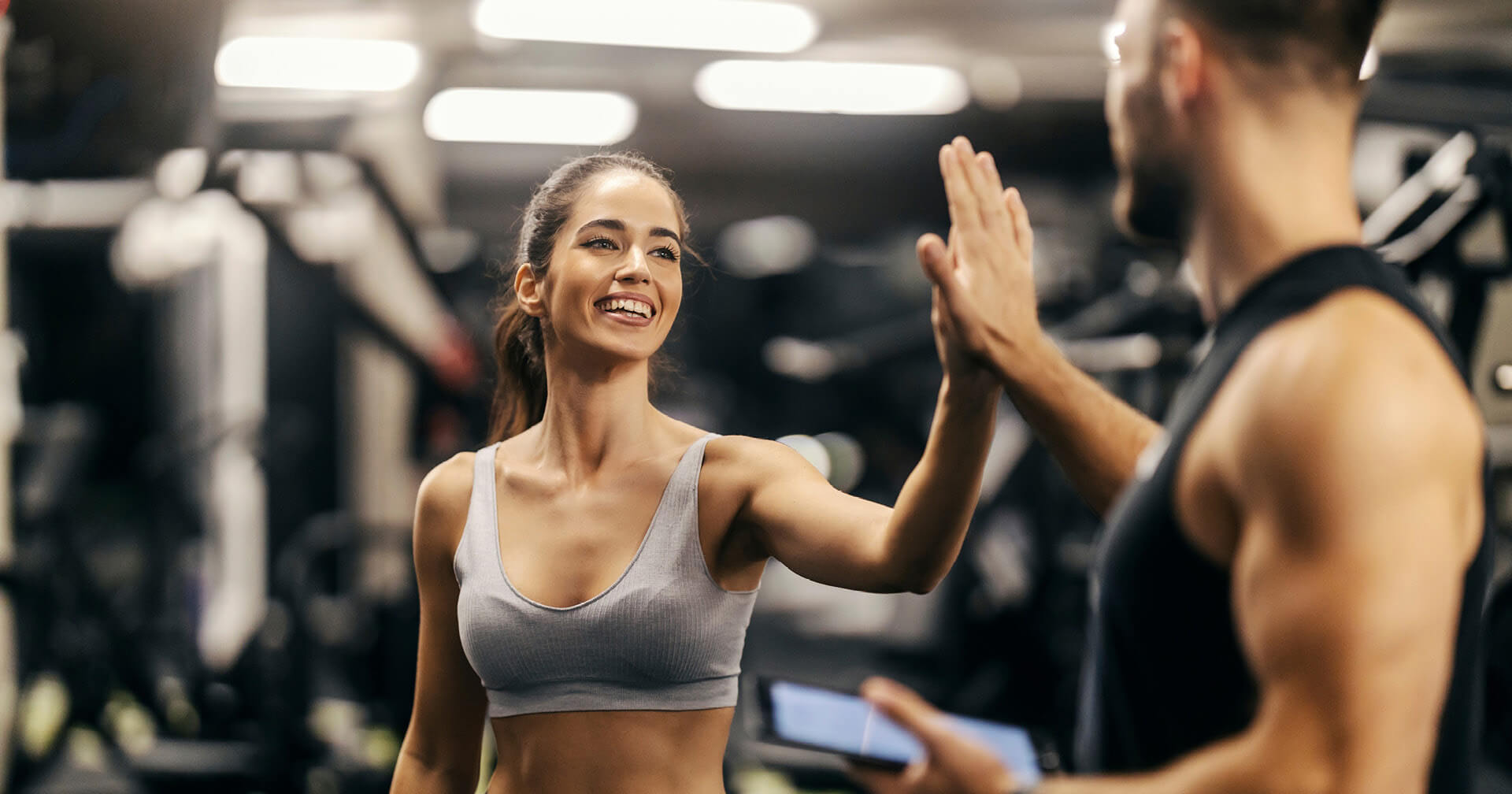 Fröhliche Frau High Five im Gym mit Trainer