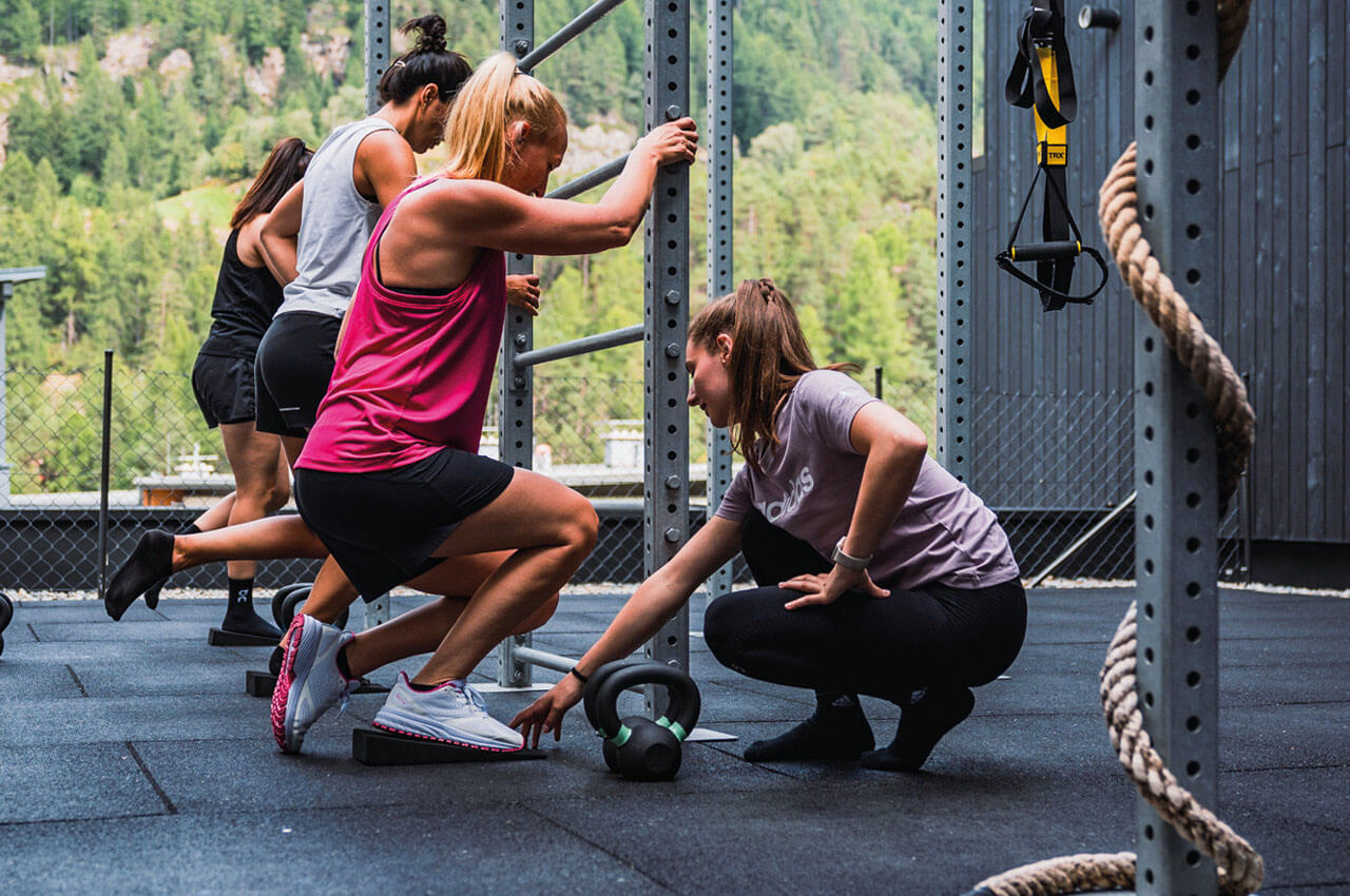 Frauen trainieren gemeinsam im Outdoor-Bereich eines Fitnessstudios mit Bergpanorama, w&auml;hrend eine Trainerin Anweisungen gibt