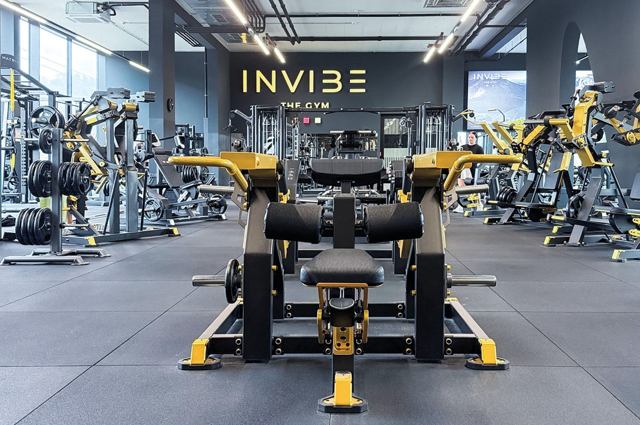 Modern ausgestattetes Fitnessstudio mit Kraftger&auml;ten, Gewichten und Maschinen in schwarz-gelber Farbgestaltung, im Vordergrund eine Trainingsmaschine.