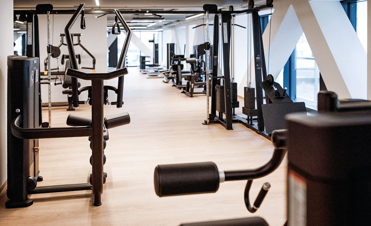 Heller Fitnessraum mit modernen Kraftger&auml;ten und Trainingsmaschinen auf Holzfu&szlig;boden.